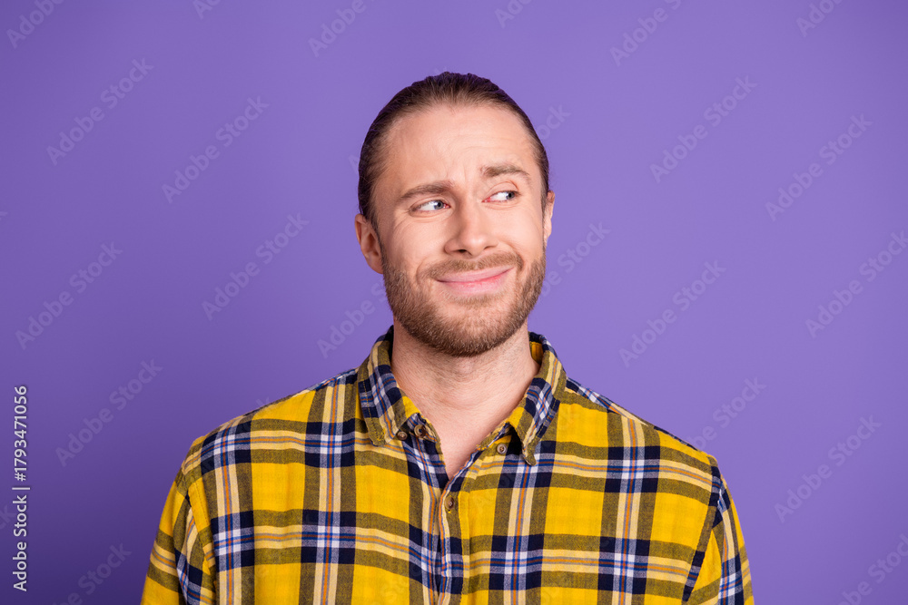 Obraz premium Young handsome man in a yellow plaid shirt smiles softly against a purple background for lifestyle fashion advertising and promotional imagery