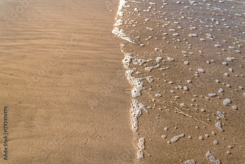 Sea foam washing over sandy beach