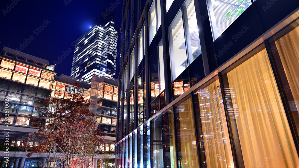 Obraz premium Modern office building in city center illuminated at night. Rows of lit windows against the architectural grid of a modern facade.