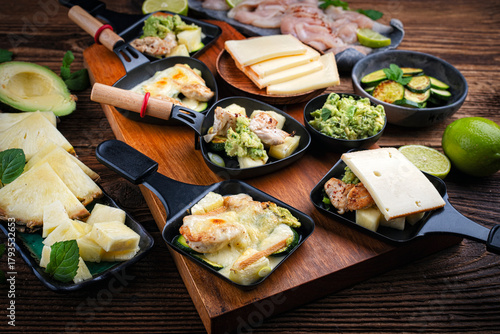 Traditional authentic Swiss raclette with chicken filet meat, pineapple, avocado and savoy cheese served as close-up on a wooden design board