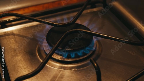 close-up gas burner with blue flame, metal grate over stainless range, low simmer and steady ignition, kitchen prep for meal, warm reflections