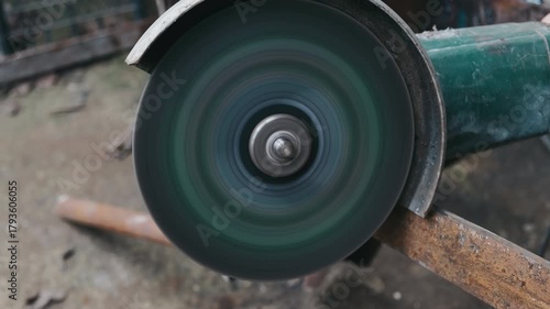 spinning grinder wheel cutting metal, close-up of disc slicing pipe with abrasive edge, blurred rotation and debris shower, handheld tool with guard