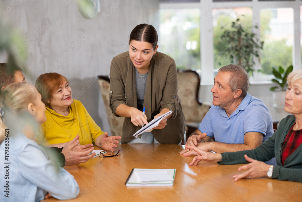 Fototapeta premium Emotional young female tutor leading educational class for group of older women and men..