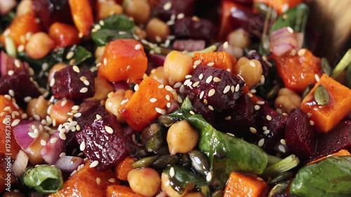 Sprinkling sesame seeds on roasted pumpkin beet chickpea salad. Close-up.