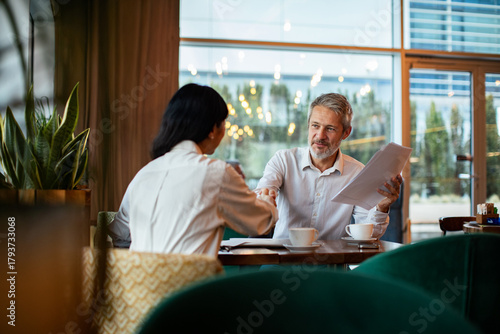 Adult man and woman shaking hands in friendly modern cafe meeting