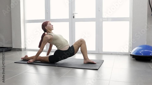 Morning exercises and yoga practice, a young woman stretches in a bright, spacious gym. A female athlete demonstrates exercises