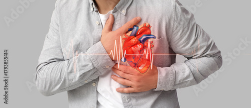 Young man suffering from heart attack on grey background, closeup