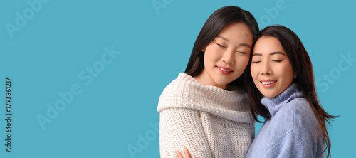 Beautiful young happy Asian sisters hugging on blue background