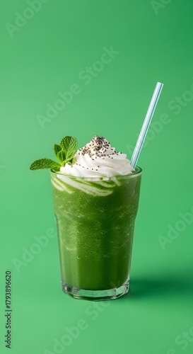 A vibrant green smoothie topped with whipped cream, chocolate sprinkles, and fresh mint leaves against a matching green background