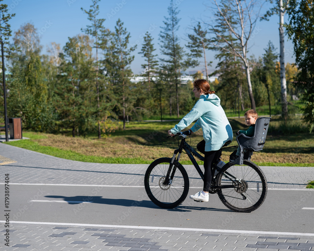 Obraz premium Caucasian woman rides bicycle with one-year-old son in park. 