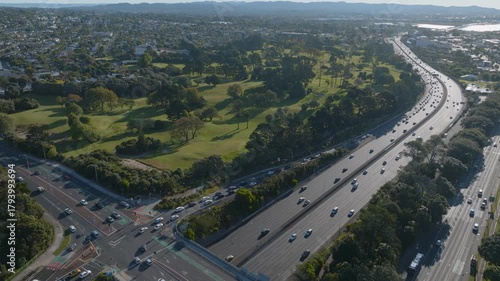 Aerial view of Auckland, New Zealand, showing a busy highway with cars moving in both directions. Chamberlain golf course and residential area are adjacent to the highway.