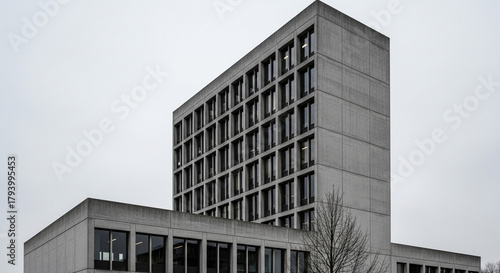 A tall, brutalist building rises against a cloudy sky, its concrete facade punctuated by rows of windows, a testament to modern architecture and urban design