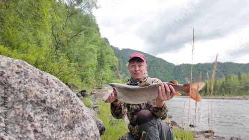 Female fisher celebrates a successful catch in the mountains — close-up of the taimen’s vivid tail and open mouth, with forested slopes behind, until it slips free, drops to the ground