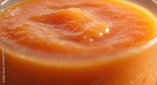 Bright orange fruit puree exhibits a thick, textured surface with shimmering highlights