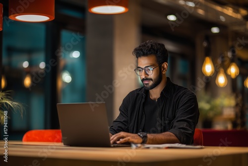 Smiling indian business man working on laptop at home office. Young indian student or remote teacher using computer remote studying, virtual training, watching online education webinar at home office.