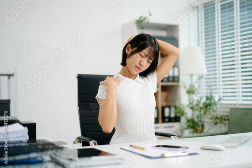 A young office woman suffering from neck and back pain while working at her desk, showing workplace stress, poor posture, and the need