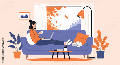 A woman relaxes on a cozy sofa at home, enjoying a warm drink while working on her laptop with a sleeping cat nearby, framed by an autumn window view.