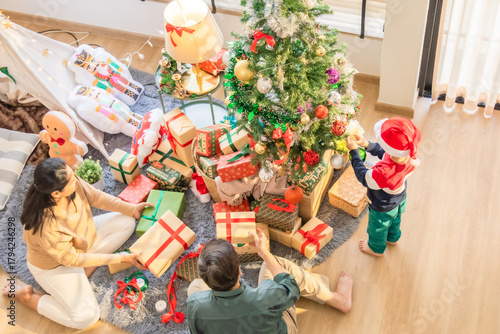 Asian grandparents and child spend holiday morning decorating Christmas tree, arranging wrapped presents with ribbons, bright light and warm feeling of love, joy, and festive family lifestyle at home