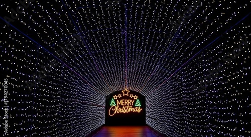 Fototapeta Naklejka Na Ścianę i Meble -  Illuminated tunnel of christmas lights leading to a merry christmas sign creating a festive atmosphere