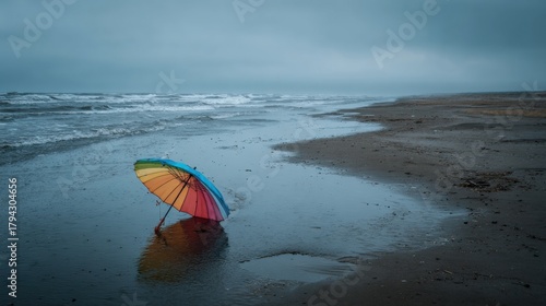 Colorful umbrella lying on deserted rainy beach under cloudy sky with soft reflection on wet sand ideal for travel melancholy visuals and weather concept designs
