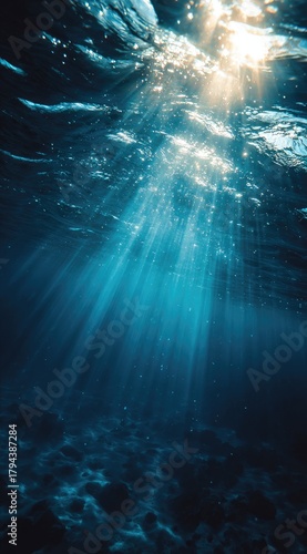 Sunbeams pierce deep ocean water, illuminating a dark, textured seabed.  Particles dance in the light shafts