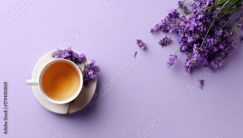 Overhead view of a cup of tea and fresh lavender blossoms on a pale purple background; teacup sits on saucer, sprigs of lavender arranged artfully