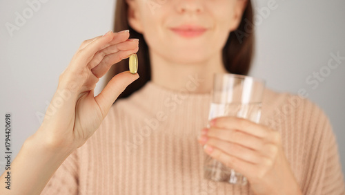 Macro close-up of an unrecognizable smiling woman holding vitamin capsule and glass of water. Advertising concept for vitamins and nutritional supplements, health care.