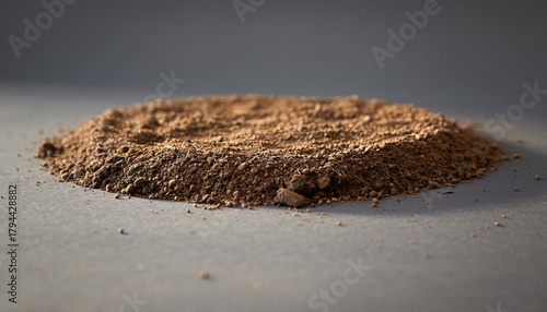 A detailed close-up of a circular pile of brown soil or dirt on a flat grey surface.