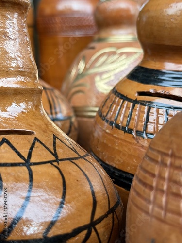 Stacked glossy clay pots show intricate black and gold painted pattern detail at marketplace