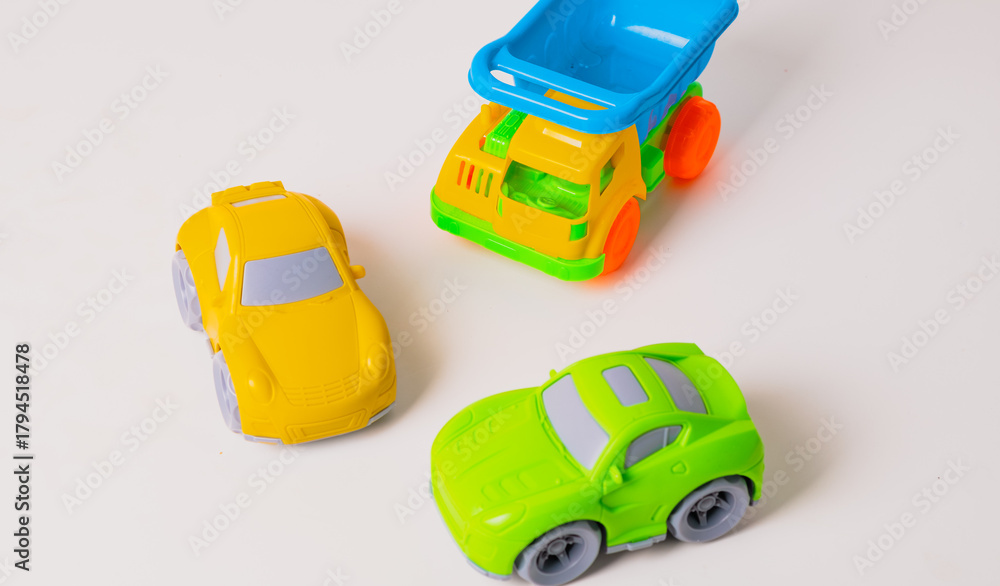 Obraz premium Brightly colored toy cars, including a green sports car, a yellow car, and a blue dump truck, are placed together on a clean surface, inviting kids to engage in imaginative play indoors.