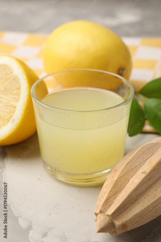 Fototapeta premium Lemon juice in glass, squeezer, leaves and fresh lemons on light grey table, closeup
