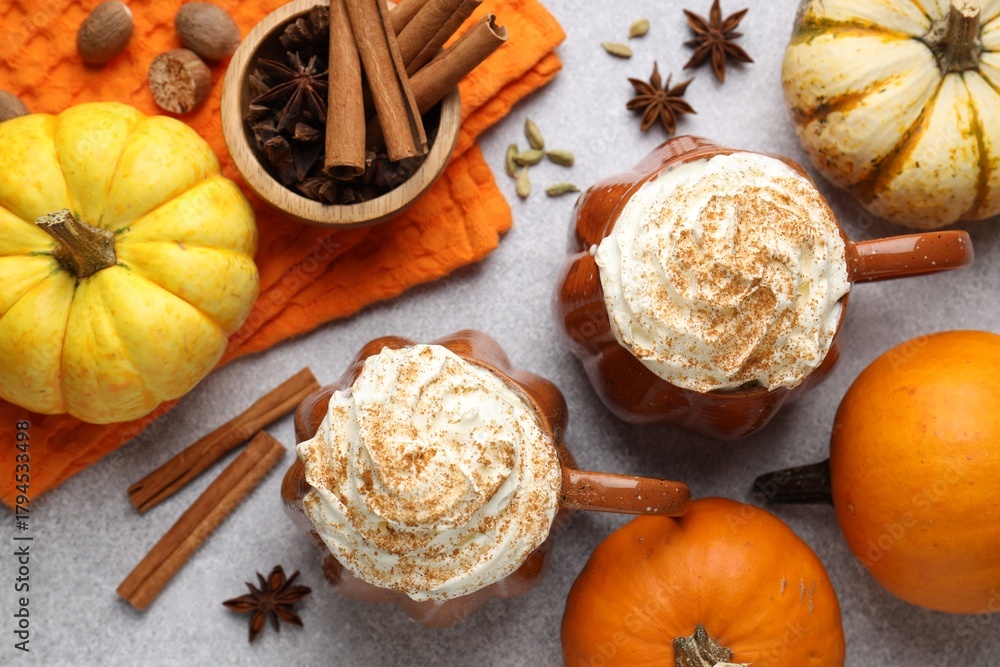 Obraz premium Tasty pumpkin latte with whipped cream in cups, spices and ingredients on light grey table, flat lay