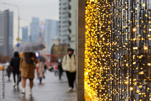 Christmas lights on electric garlands in a shop window on a city street. New Year decorations, people walking with umbrella