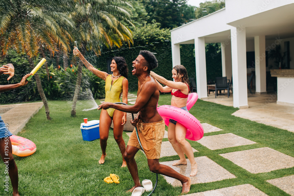 Obraz premium Friends celebrate backyard water fight and pool party
