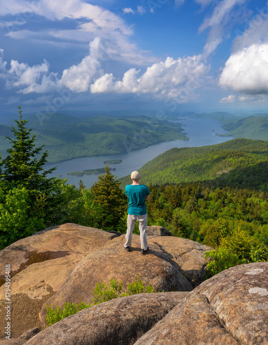 Hiker stands on Black Mountain, enjoying a scenic view of Lake George and the surrounding Adirondack landscape in New York State, USA.