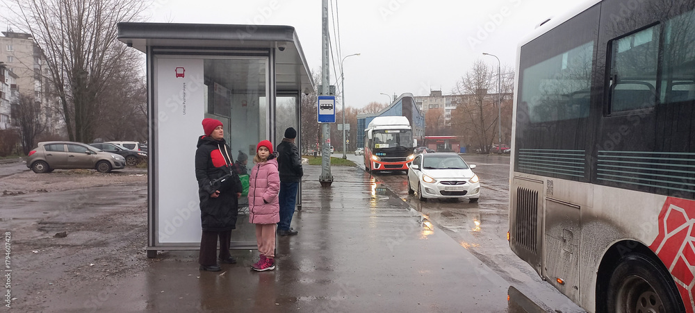 Fototapeta premium Adults and child waiting at bus stop on rainy day in city 