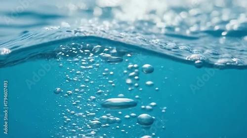 An engaging underwater perspective reveals a dynamic interplay of effervescent bubbles ascending rapidly through clear, vibrant blue water towards the agitated surface. The crisp visual detail capture