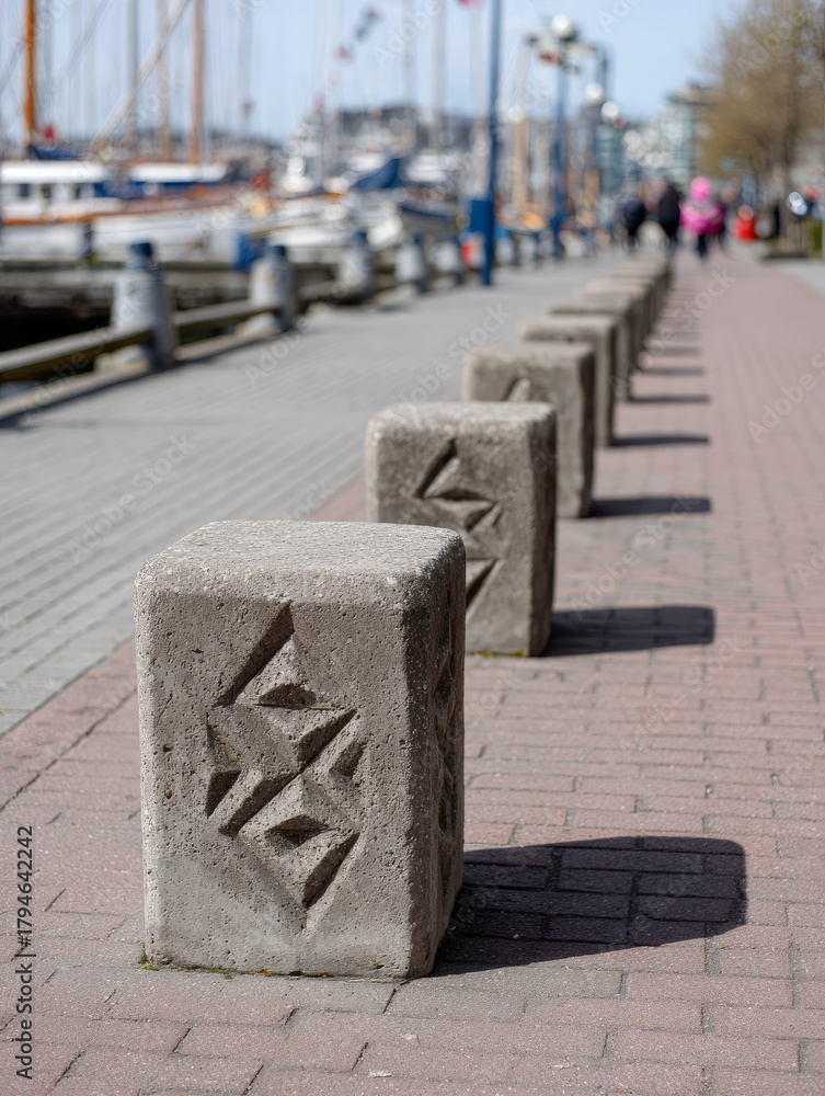 Fototapeta premium Stone bollards line a marina pathway with boats in the background.