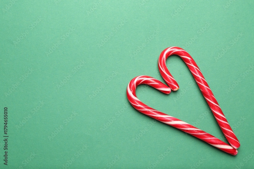 Fototapeta premium Heart made of candy canes on green background, top view with space for text. Merry Christmas and Happy New Year