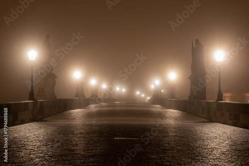 Charles Bridge over the Vltava River in Prague, Czech Republic, Shrouded in Morning Fog at Sunrise with Glowing Street Lamps, Empty of People, Creating a Calm and Atmospheric Cityscape