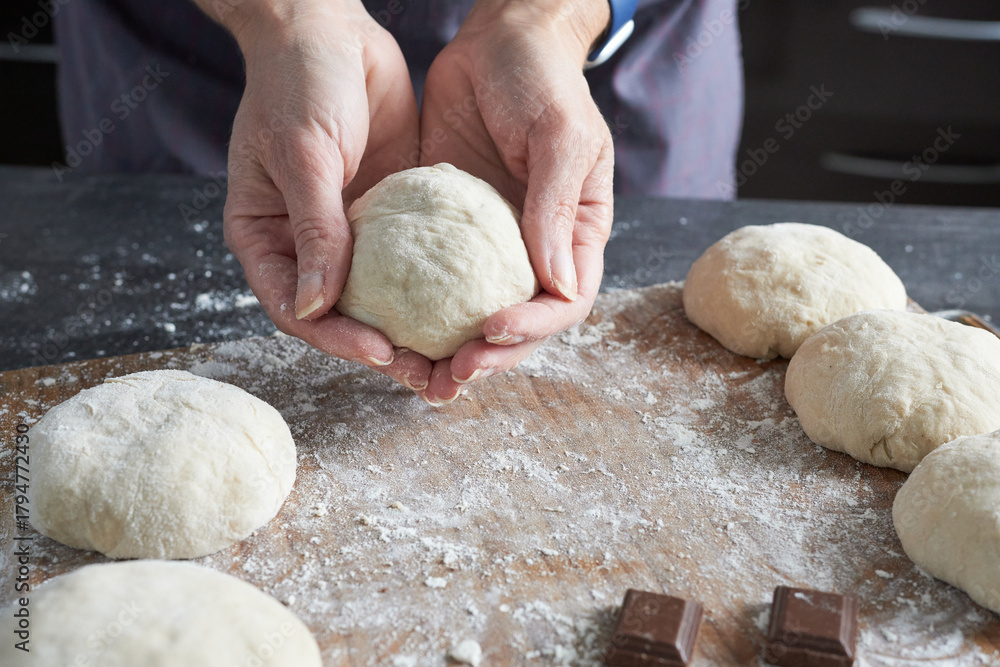 Obraz premium A close-up of a woman's hands kneading dough on a kitchen counter. Making vanilla buns.