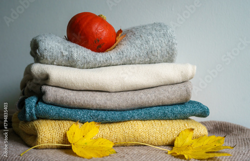 Autumn still life - a stack of sweaters, a pumpkin and yellow maple leaves on a knitted blanket.