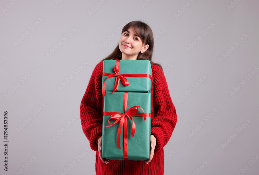 Fototapeta premium Beautiful woman in red sweater with gift boxes on grey background. Christmas and New Year celebration