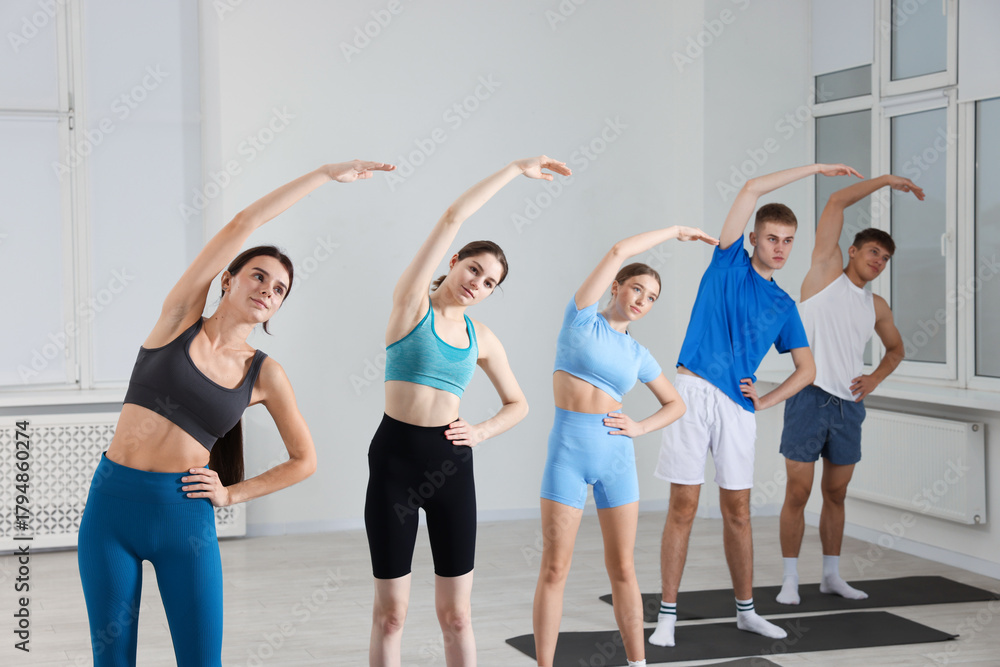 Naklejka premium Group of people doing stretching exercise on fitness mats in gym