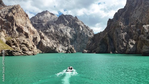 A small boat glides across the stunning turquoise waters of Kel-Suu lake in Kyrgyzstan, surrounded by dramatic mountain scenery.