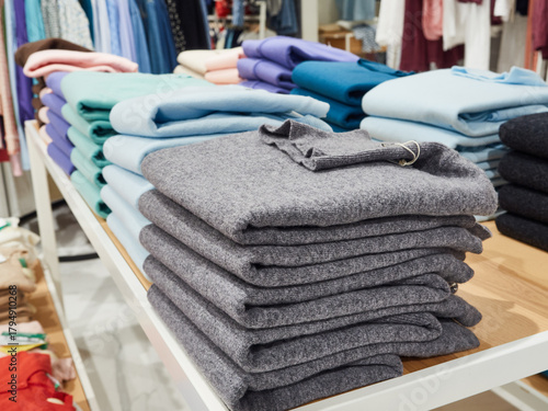 Multicolored T-shirts are stacked on the shelves of a clothing store for sale