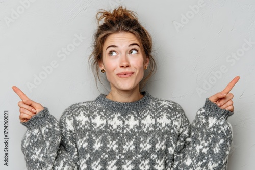 A young attractive woman in a winter sweater at home looks up in astonishment pointing with raised arms
