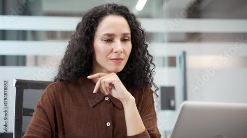 Busy businesswoman working on laptop and thinking about task while sitting at workplace in modern business office. Thoughtful female employee deals with project on computer or chats online. Close up