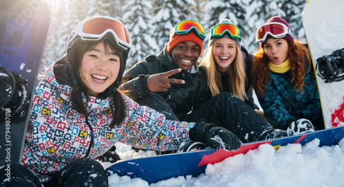 A diverse group of happy young friends sitting in the snow with snowboards and posing for a group photo. Multiethnic snowboarders enjoying a winter vacation on a sunny mountain