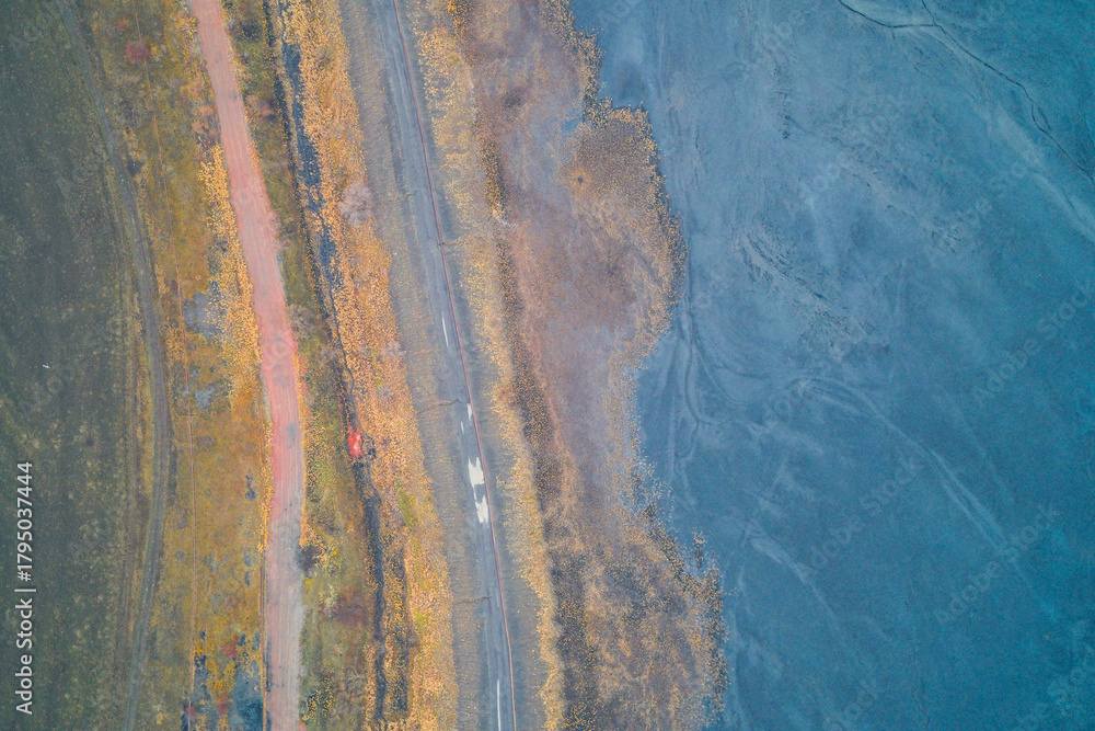 Obraz premium Drone aerial shot capturing an abstract texture of an industrial landscape. Strong contrast between warm, earthy tones of dirt gravel old road and cool blue and grey colors of sludge toxic waste area